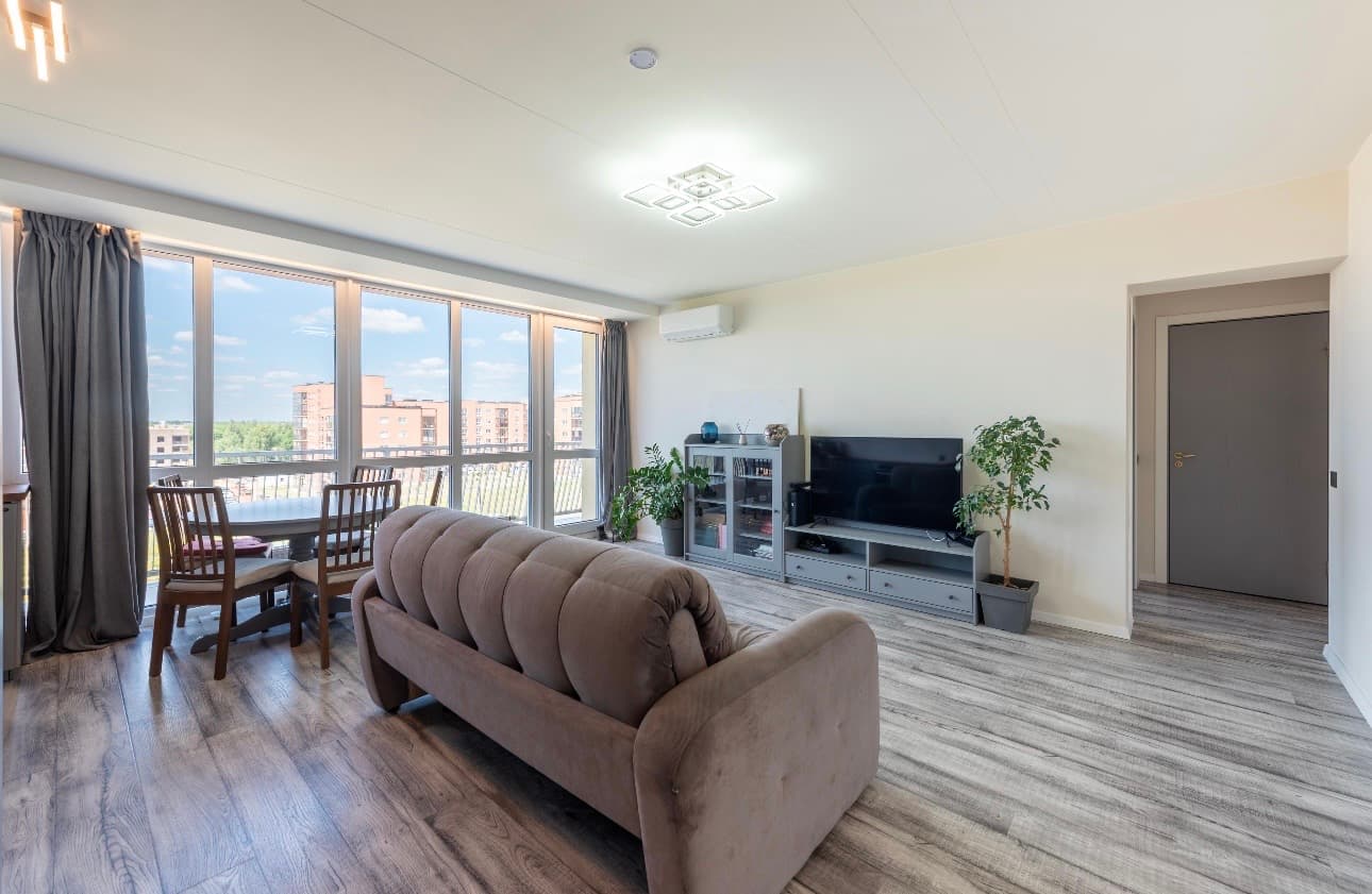Modern living room with tufted sofa, dining area, and large windows with city views.