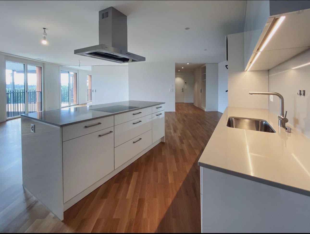 Modern white kitchen with a large island, stainless steel range hood, and hardwood floors.