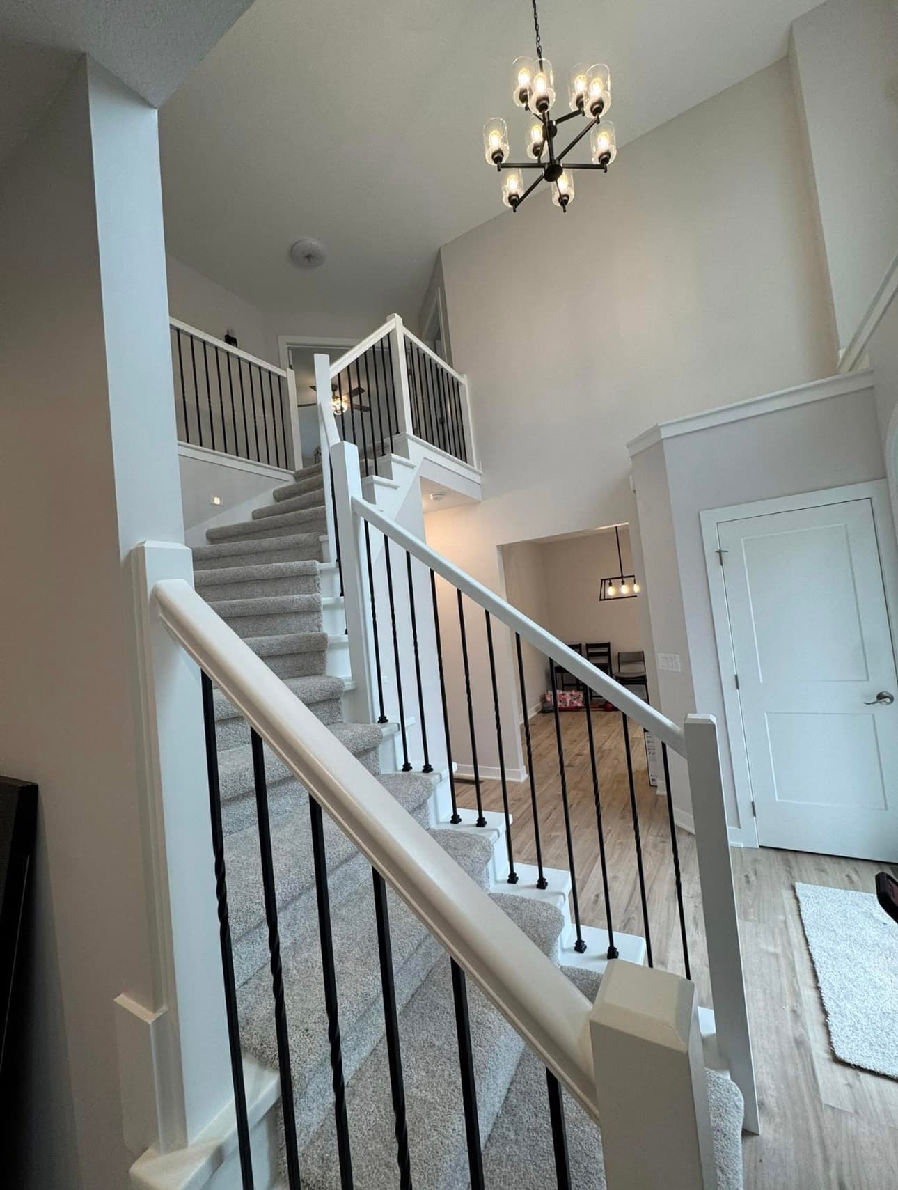 Carpeted staircase with white banisters and black spindles under a modern multi-bulb chandelier.