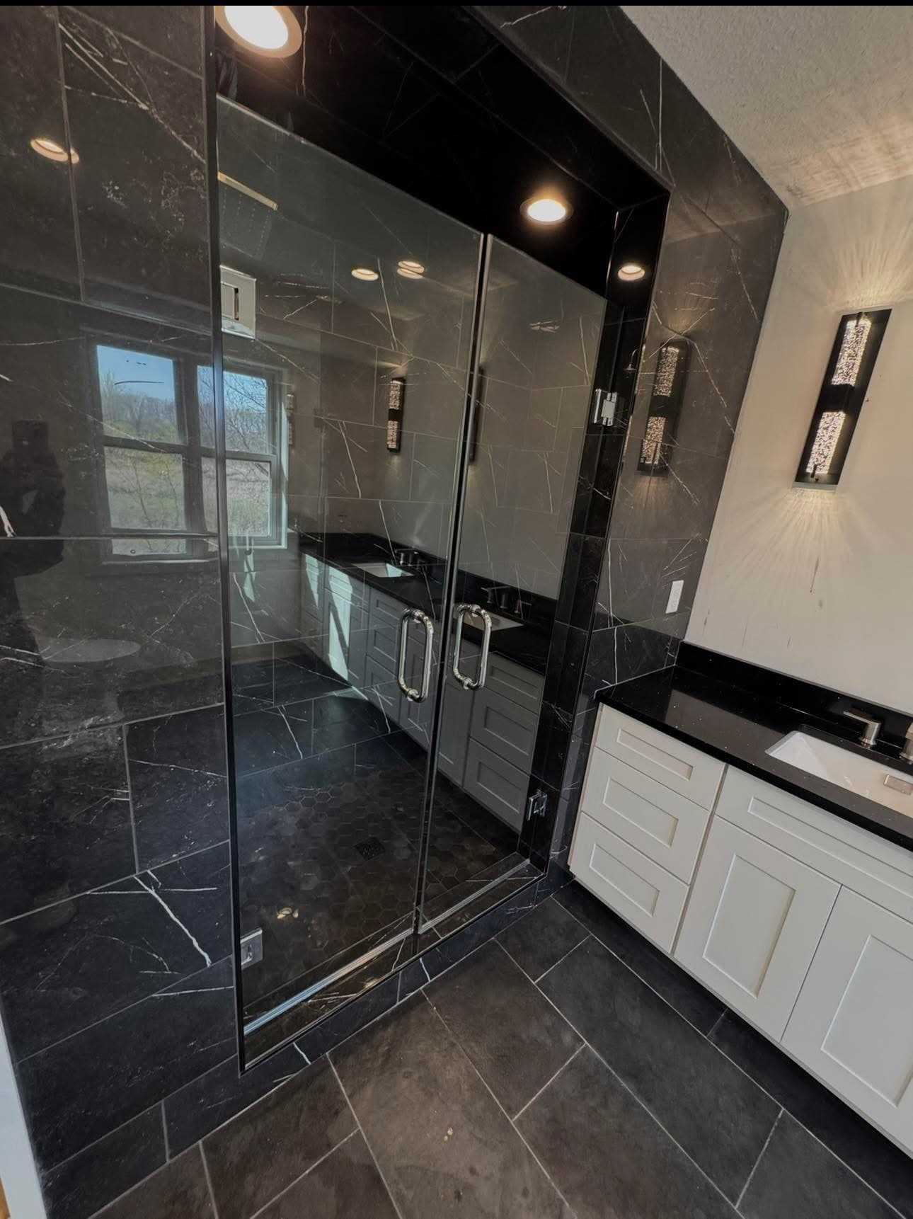 Modern bathroom with black marble shower walls, glass doors, and white vanity with black countertop.