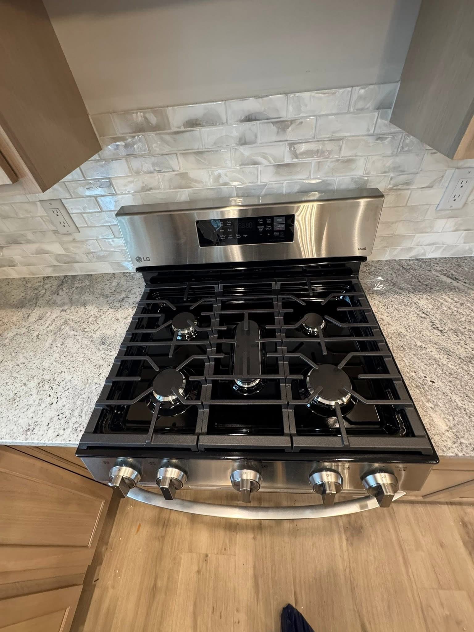 Stainless steel LG gas range with five burners, white marble backsplash, and granite countertop.